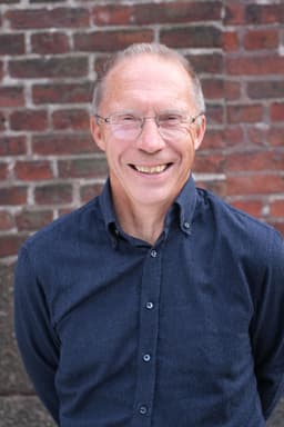 Lars Carlson har blå skjorta och glasögon och skrattar.